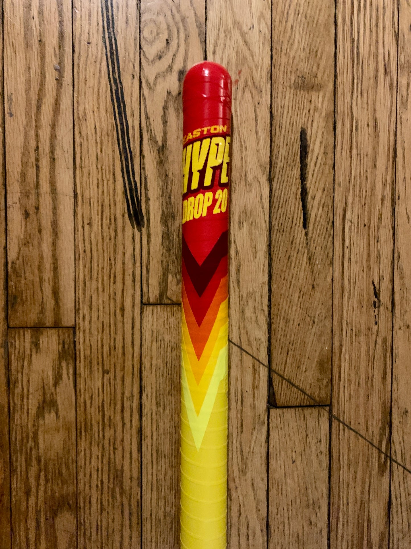 Custom wrapped yellow and red WIFFLE bat with chevron pattern on wooden floor